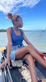 Young woman sitting on lounge chair at beach against sky