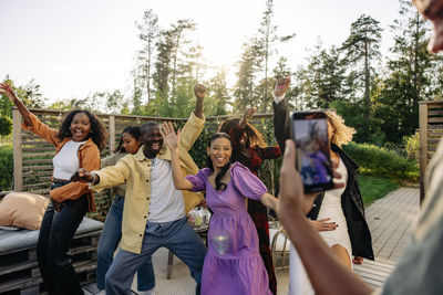 Man photographing cheerful male and female friends dancing during party in back yard