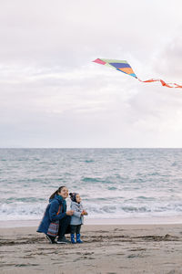 Rear view of woman sitting on beach against sky