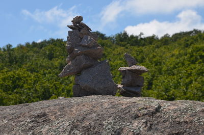 Stone stack on rock by trees against sky