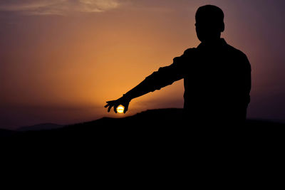 Optical illusion of silhouette man holding sun during sunset