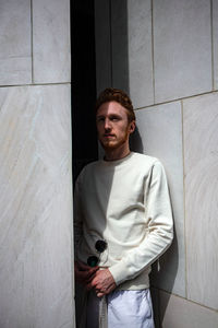 Portrait of young man leaning against wall at home