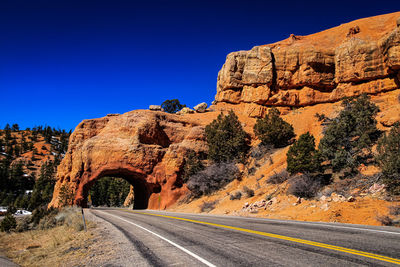 Road by rock formation against clear blue sky