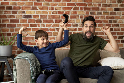 Portrait of young friends using mobile phone while sitting against wall