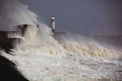 Lighthouse amidst sea and buildings against sky