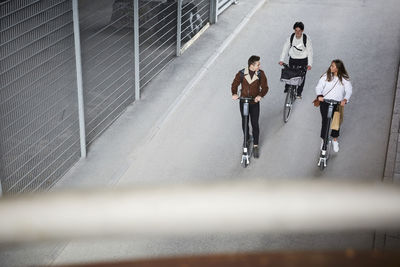 High angle view of teenage friends riding electric push scooters and bicycle on road in city