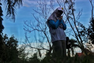 Low angle view of woman wearing hijab and cap standing against sky during dusk