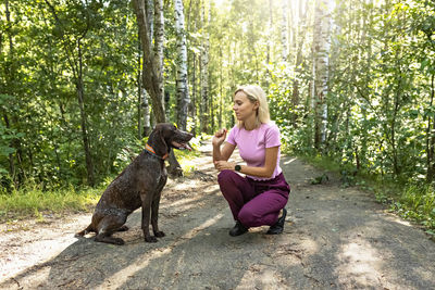 Portrait of a young blonde woman training a hunting dog of the kurz-haar breed in the park. summer 