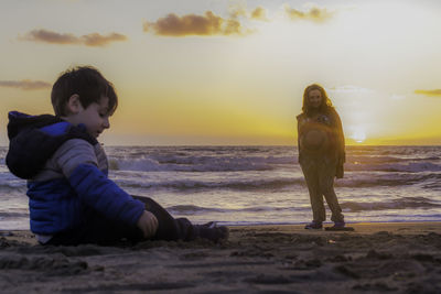Full length of woman and boy on beach against sky during sunset