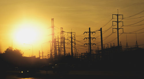 Silhouette electricity pylons against sky during sunset