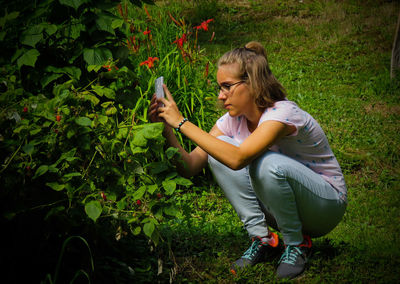 Teenage girl photographing plants while crouching on field