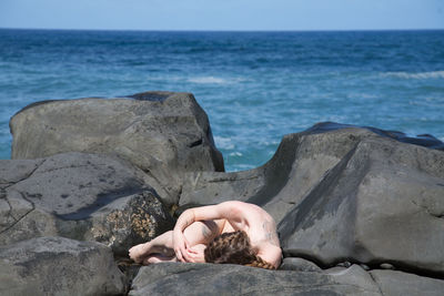 Low section of man on rock by sea against clear sky