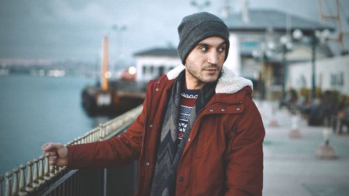 Young man in warm clothing looking away while standing by railing