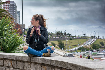 Young woman photographing while sitting on retaining wall