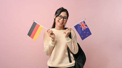 Portrait of young woman holding gift against pink background