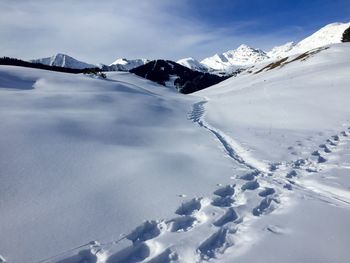 Ski tracks on snowcapped mountain against sky