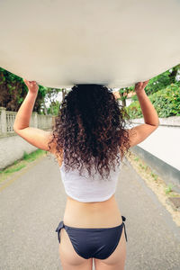 Rear view of woman carrying surfboard on road