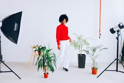 Woman standing by potted plants against wall