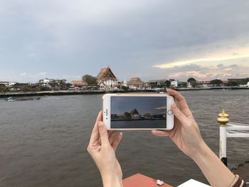 Midsection of woman photographing sea against sky