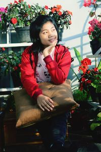 Portrait of smiling young woman sitting by potted plant