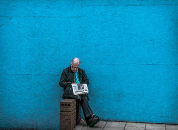 Portrait of man sitting against blue wall