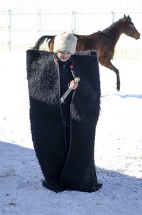 Boy standing in sleeping bag with horse in background during winter