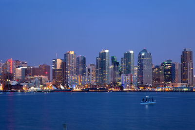 Sea by illuminated city against clear blue sky