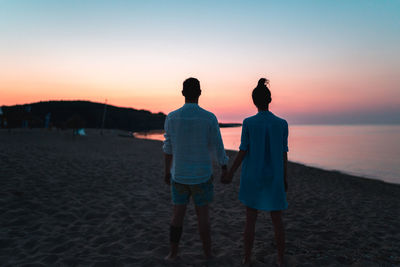 Rear view of friends on beach against sky during sunset