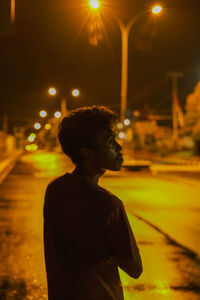 Side view of young man looking at illuminated city street