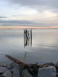 Wooden posts on rocks by lake against sky