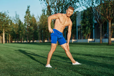 Full length of shirtless man exercising on field