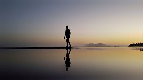 Silhouette man walking on shore against sky during sunset