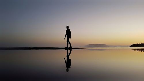 Silhouette man standing in sea against sky during sunset