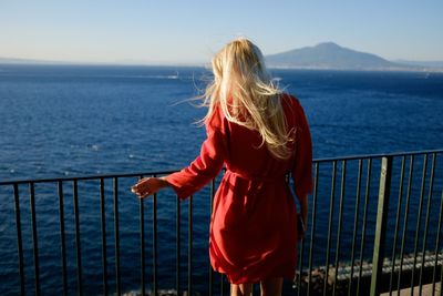 Rear view of woman standing by railing while looking at sea