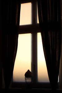 Silhouette lamp against sky seen through window