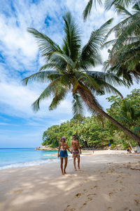 People on beach by palm trees against sky