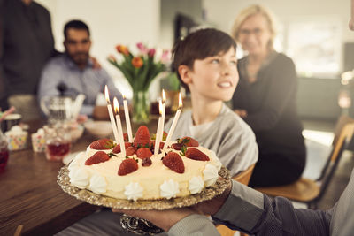 Close-up of grandfather holding birthday cake with family in background