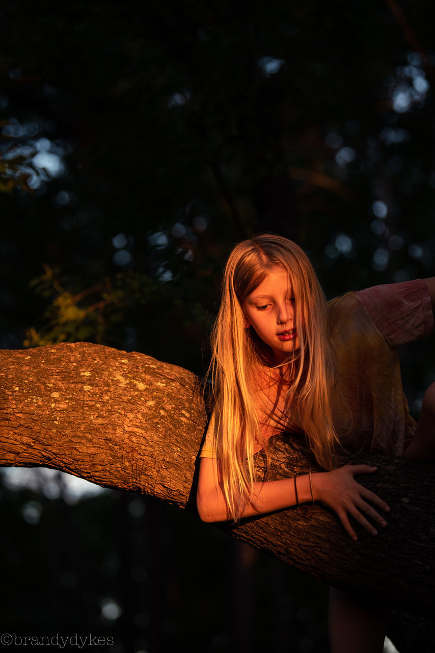 BEAUTIFUL YOUNG WOMAN SITTING AGAINST TREE