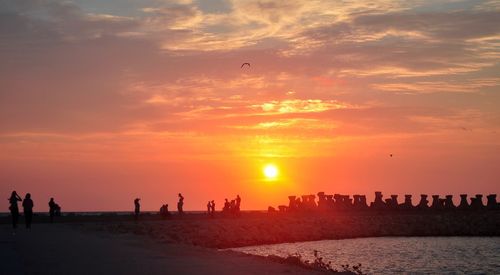 Silhouette people on beach against sky during sunset