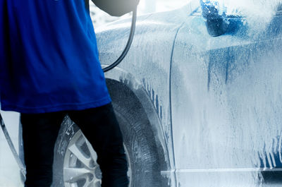 Worker washes blue suv car with soap foam. exterior carwash. car care business. vehicle cleaning.