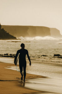 Rear view of surfer walking at beach