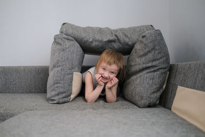 Kid toddler builds house from pillows on sofa in living room, lifestyle and games in real interior