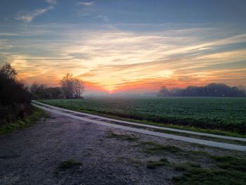 Road by landscape against sky during sunset