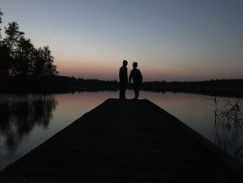 Silhouette people standing on lake against sky during sunset