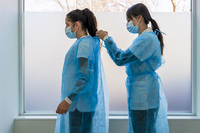 Nurse helping doctor in wearing protective workwear in clinic