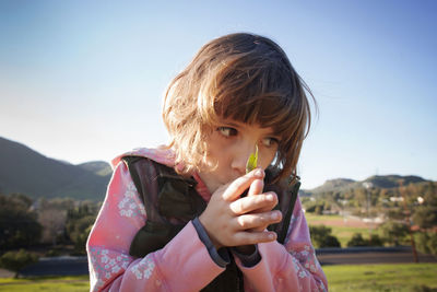 Close-up of girl with hands clasped on field against clear sky