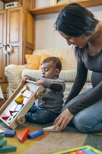 Mother looking at cute son playing with toys at home
