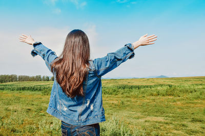 Rear view of woman with arms raised standing on field against sky