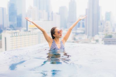 Portrait of young woman in swimming pool against buildings in city