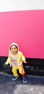 Portrait of a smiling girl standing against red wall